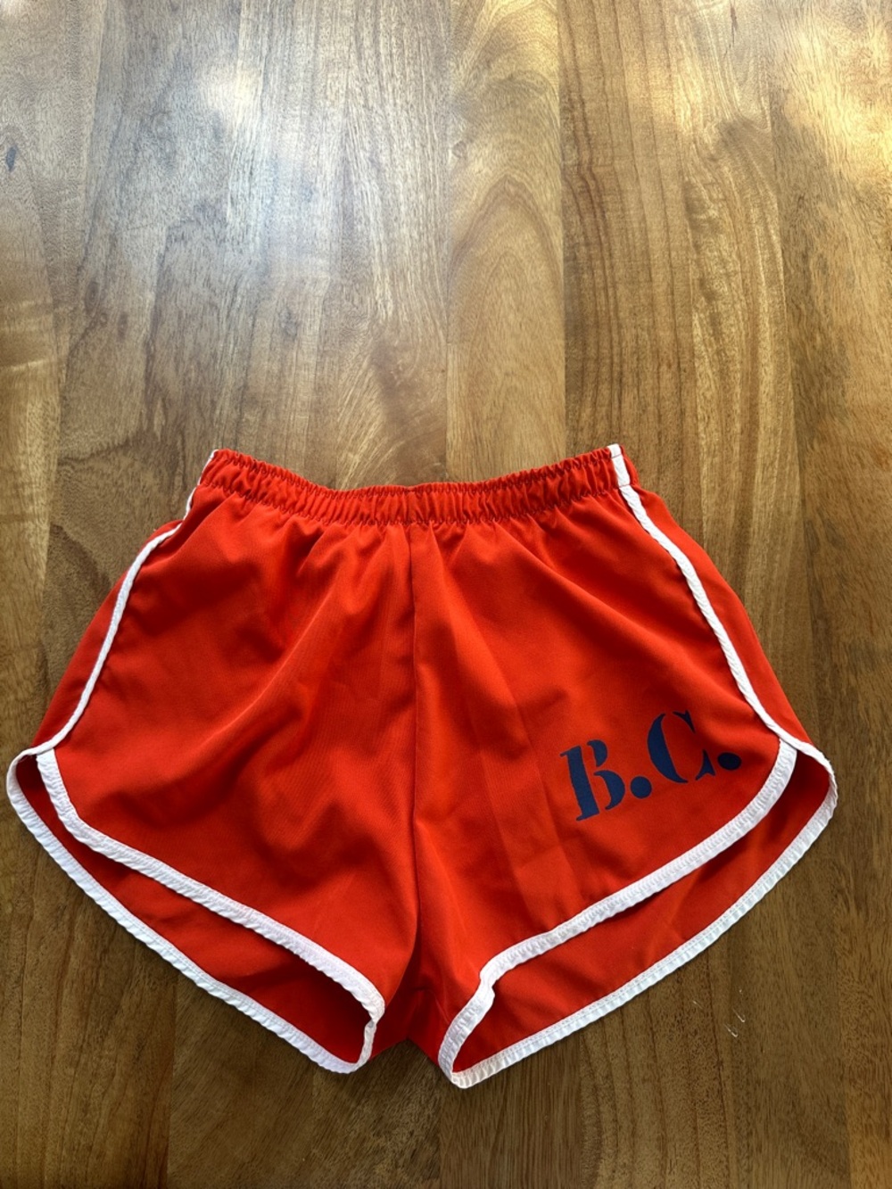Bobo Choses Red Swim Trunks with navy B.C. logo on bottom left leg